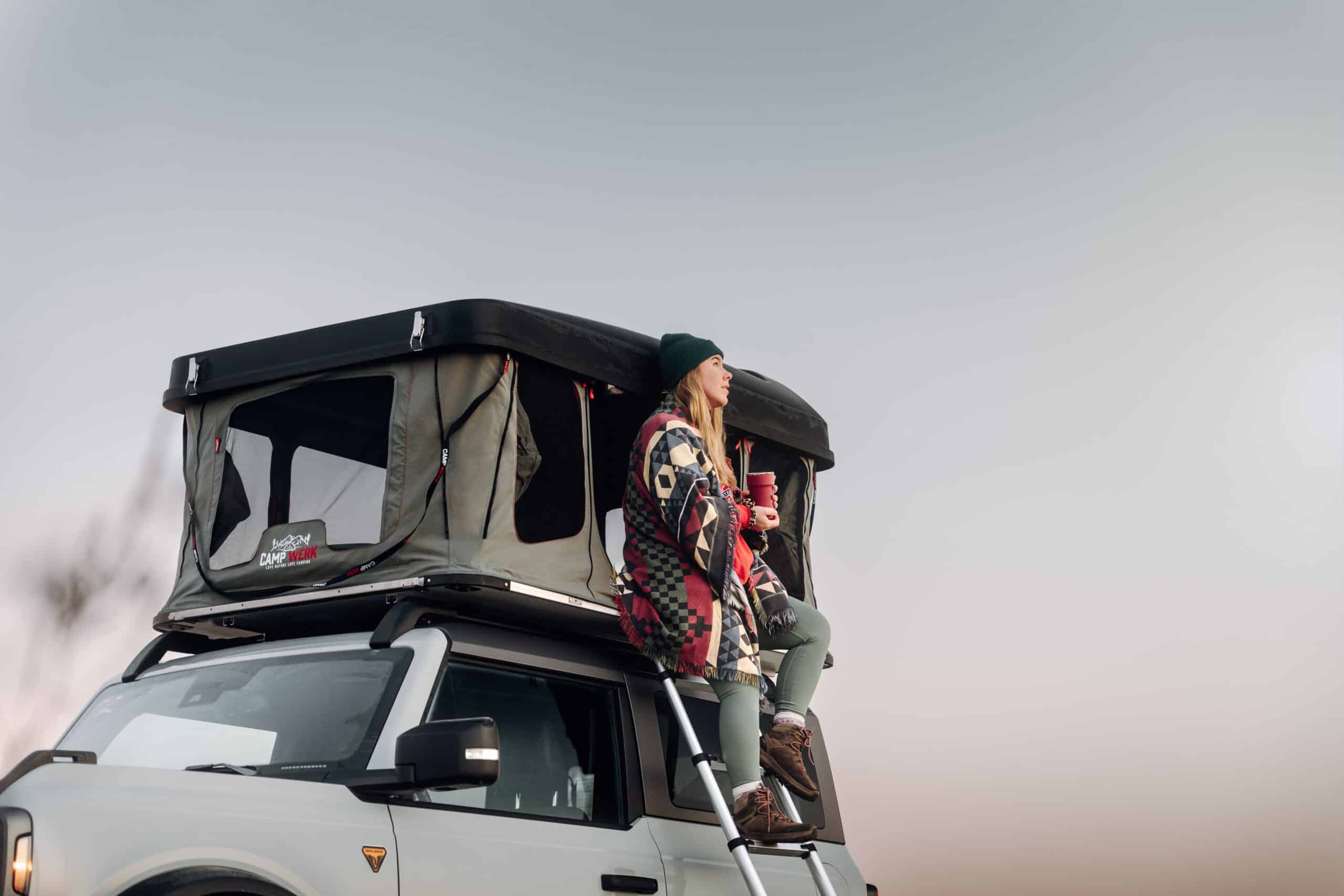 En kvinde sidder i indgangen til sit tagtelt og nyder naturen. I Good Vibes er der nok plads til det, for det byder på overraskende meget hovedhøjde. Good Vibes er det første lodret åbnende hard shell-tagtelt fra Campwerk.