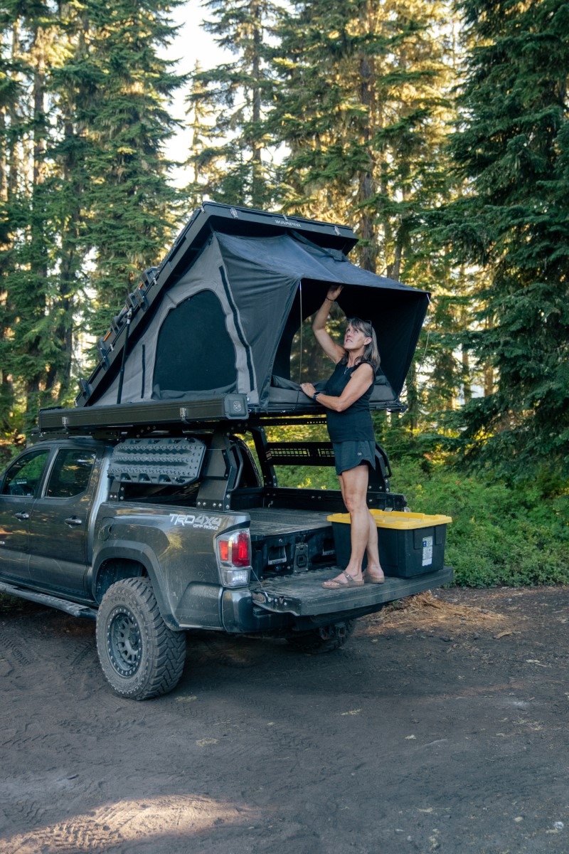 Kvinde står på ladet af sin pickup og åbner sit tagtelt 