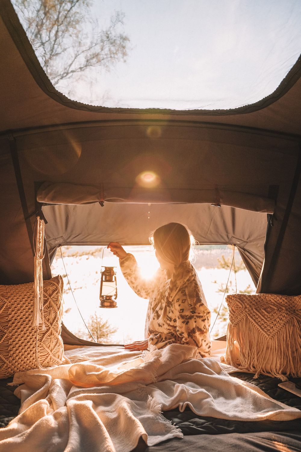 Kvinde kigger ud af åbningen på sit tagtelt i skumringen