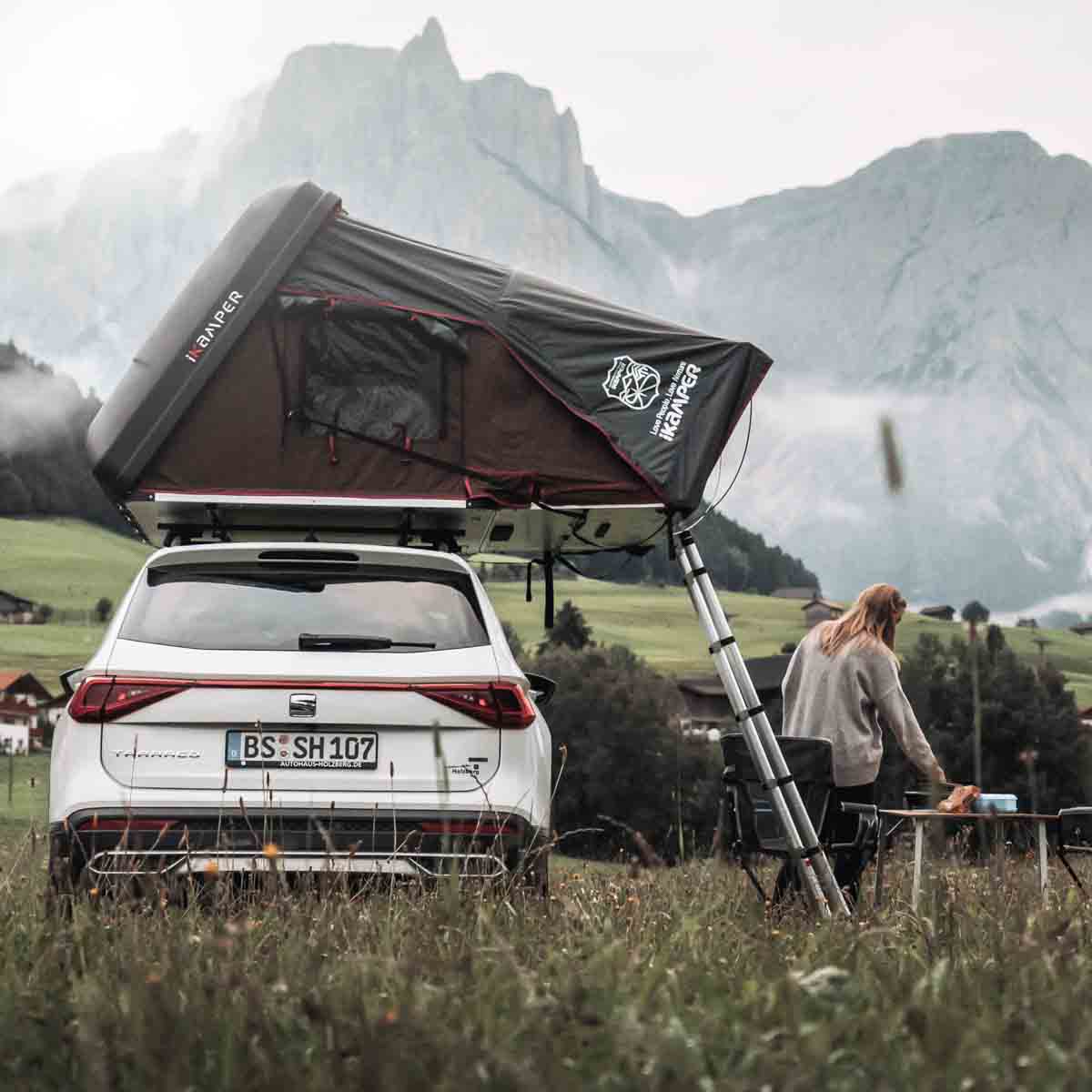 Kvinde står i bjergene ved siden af sin bil med tagtelt