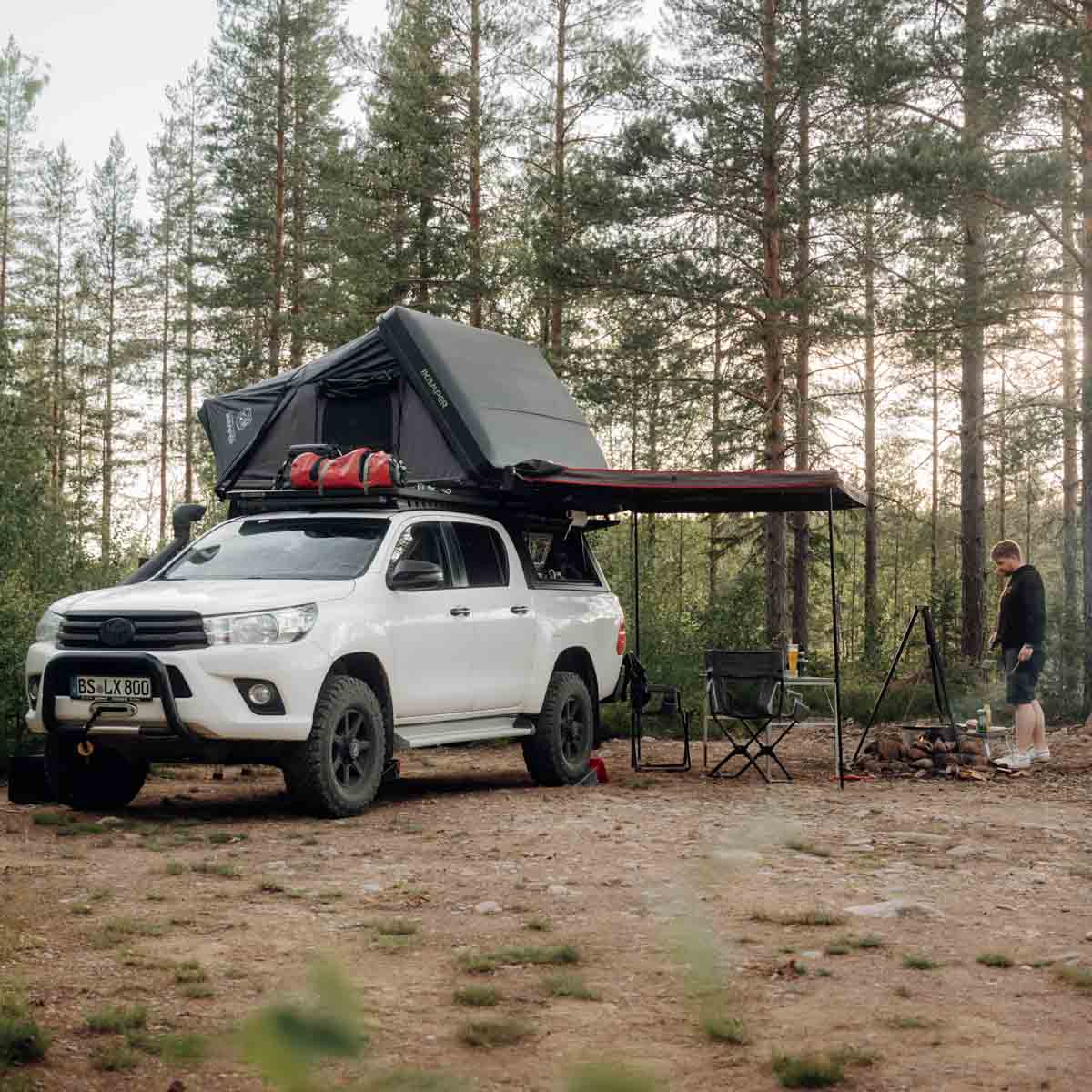 Mand camperer med sin pickup-truck med tagtelt og markise i skoven