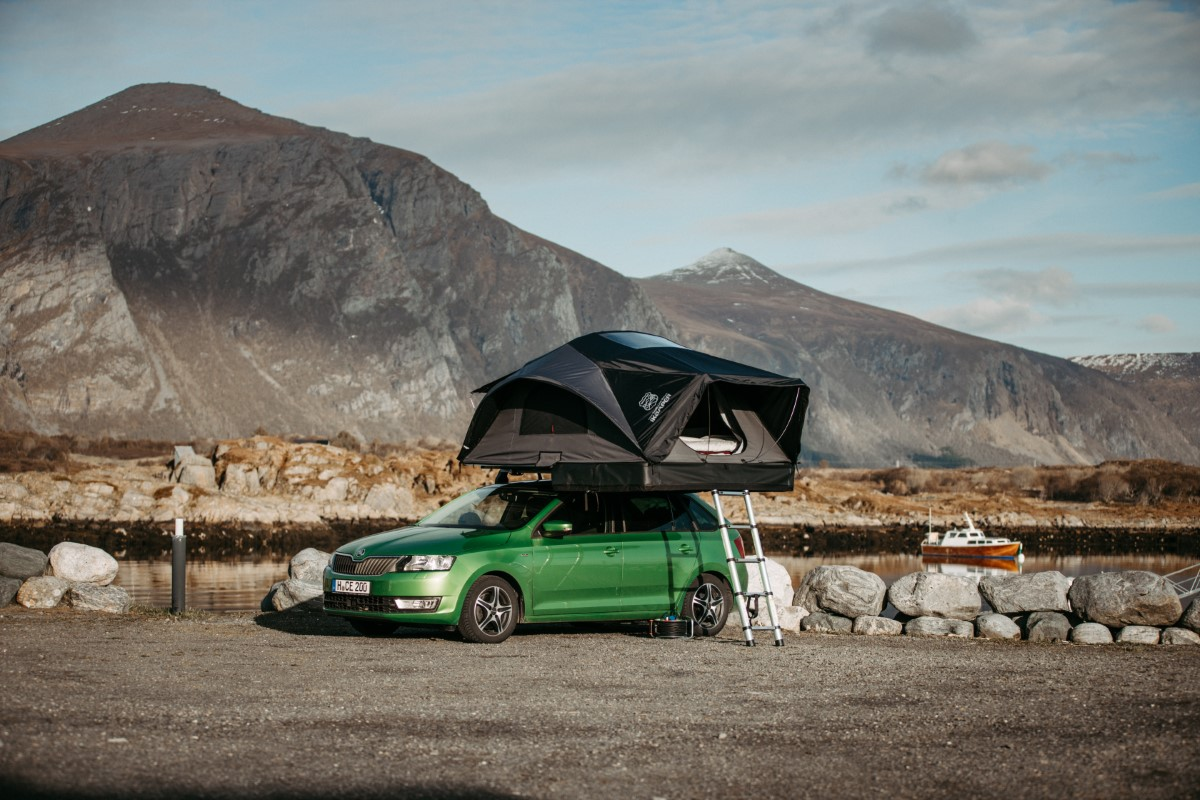 Grøn bil med X-Cover hard shell tagtelt til 1 person parkeret på en parkeringsplads i bjergene