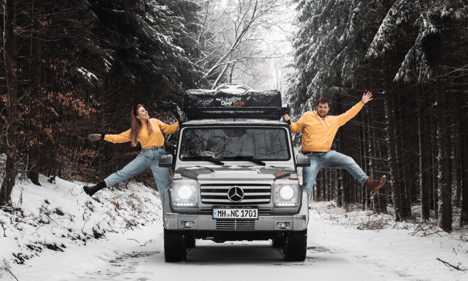  Par i matchende outfits ved siden af deres bil med Campwerk tagtelt på en sneklædt vej i skoven