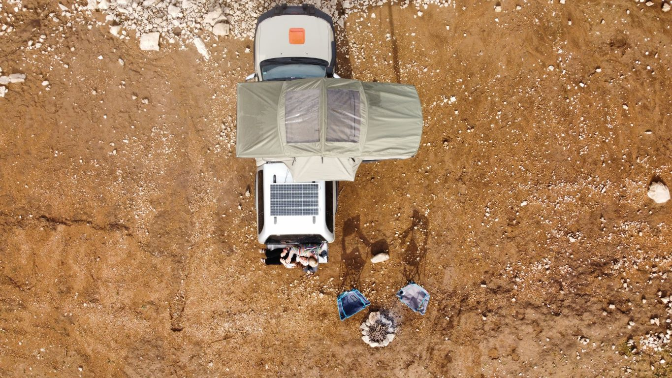 Adventure tagtelt fra Campwerk fra fugleperspektiv. Et par sidder bag på bilen, ved siden af står campingstole og et bålsted 