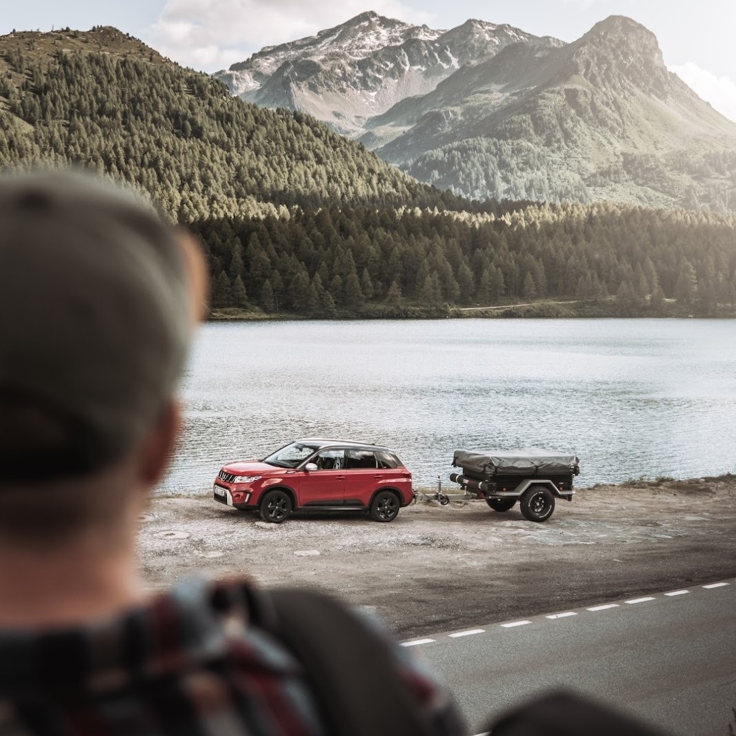 Person kigger på en bil med en afkoblet teltvogn ved søen